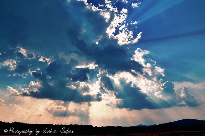 Wolken am Abendhimmel lassen die letzten Sonnenstrahlen auf die Erde fallen. Fotografie von Lothar Seifert